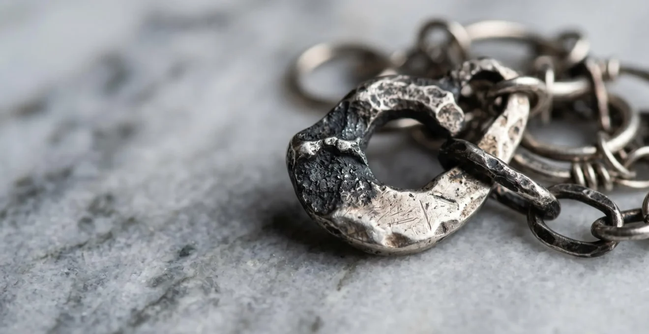 Détail artistique de bijoux en argent ternis sur surface minérale, composition mettant en valeur le contraste entre zones noircies et éclat métallique