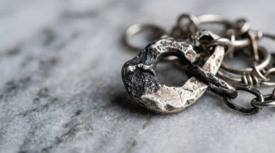 Détail artistique de bijoux en argent ternis sur surface minérale, composition mettant en valeur le contraste entre zones noircies et éclat métallique