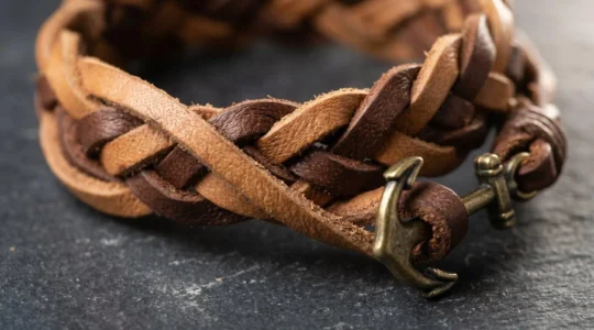 Gros plan sur un bracelet en cuir tressé marron posé sur une surface texturée, détails artisanaux visibles