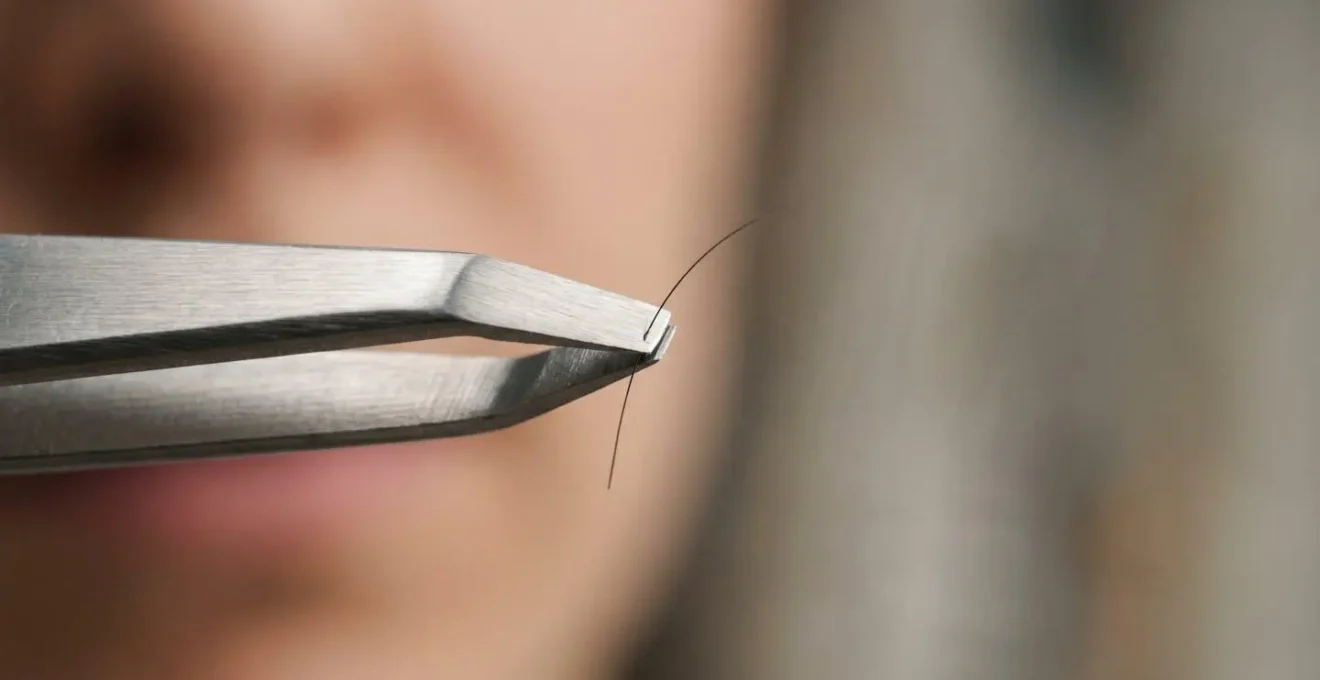 Gros plan sur une pince à épiler professionnelle tenant délicatement un poil de sourcil