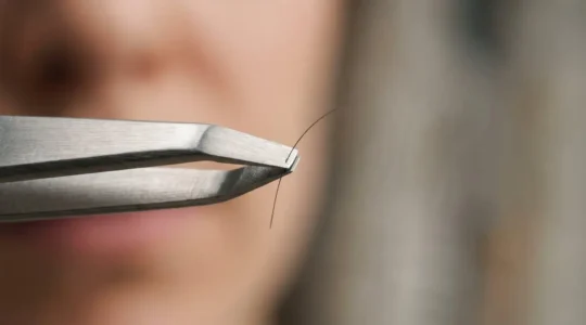 Gros plan sur une pince à épiler professionnelle tenant délicatement un poil de sourcil